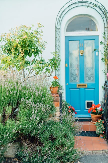 The image depicts the front garden of a property with a vibrant blue door featuring glass panels and a brass mail slot, set within a white arched frame. The garden is well-maintained, showcasing a var